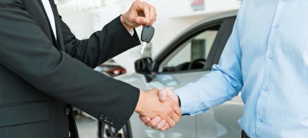 Two men shaking hands while one hands over a set of car keys in a blog post about used cars